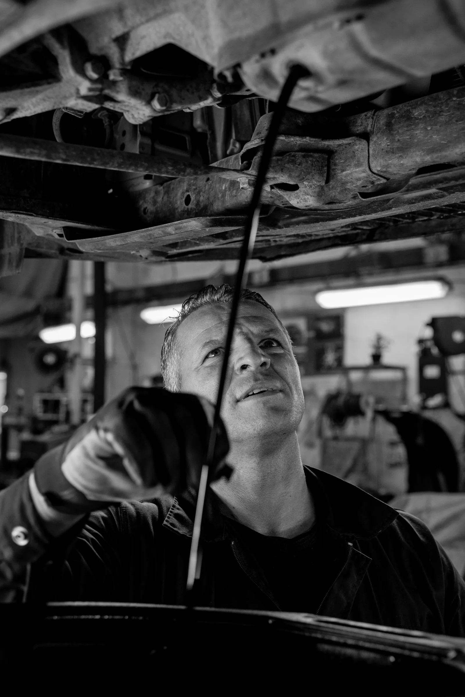 A mechanic under a raised vehicle, looking up at its underside with a work light