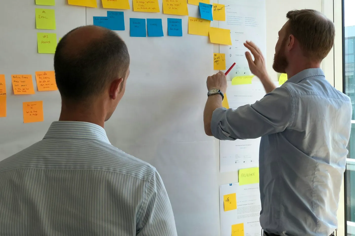 Two people mapping a workflow with sticky notes on a wall
