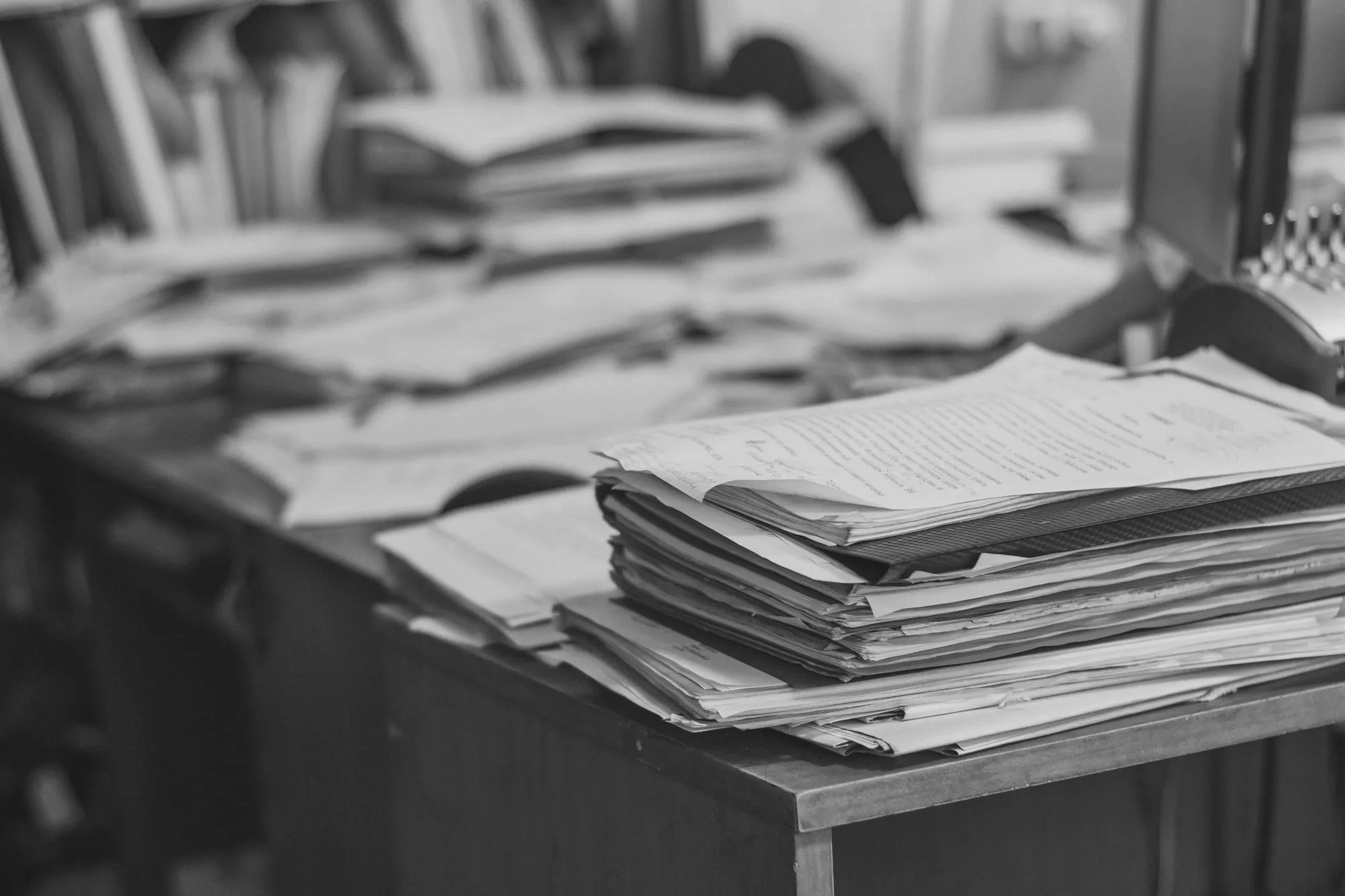 Stacks of loose paperwork piled across an office desk