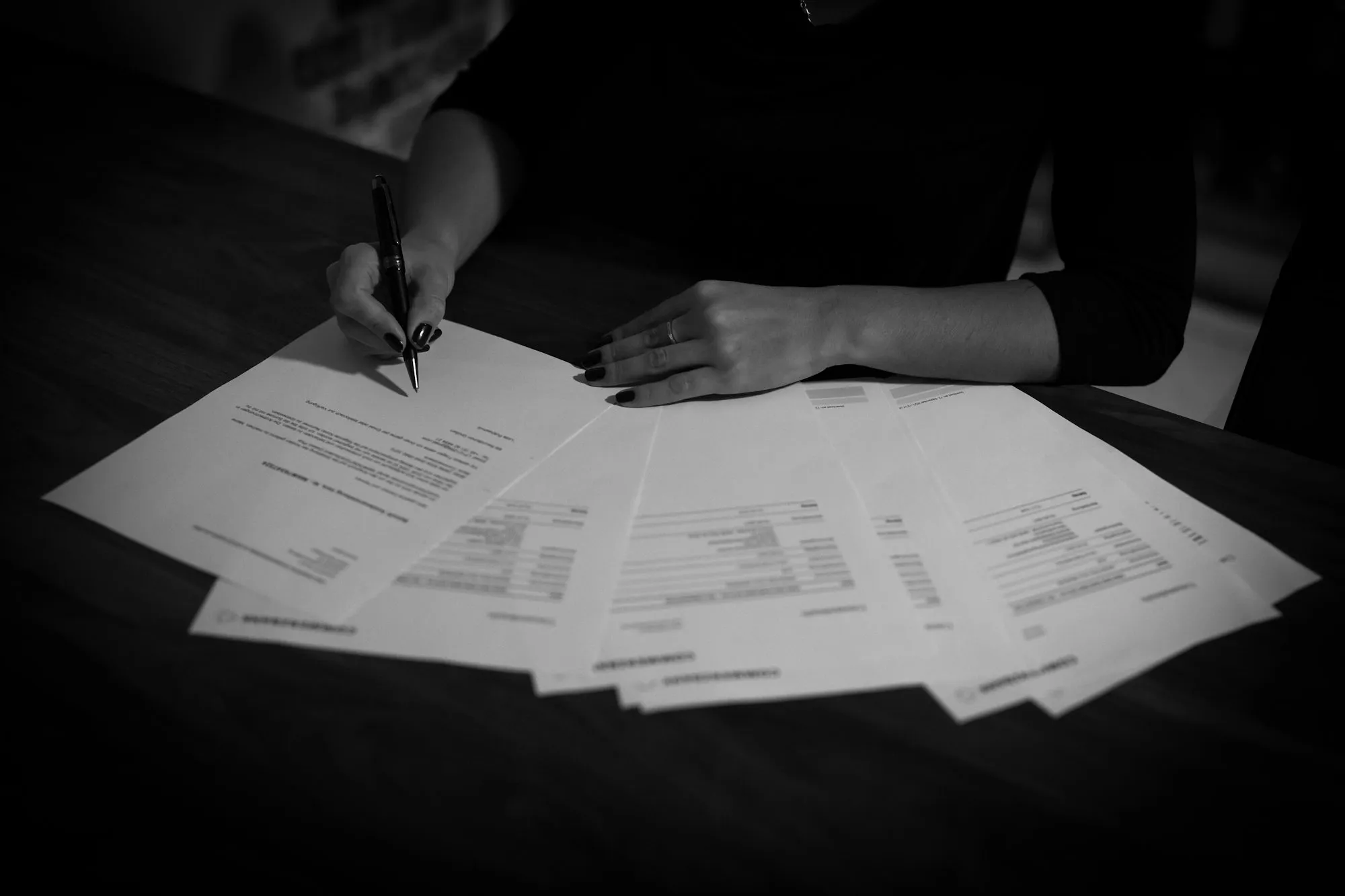 An analyst reading printed documents spread across a dark table, pen in hand