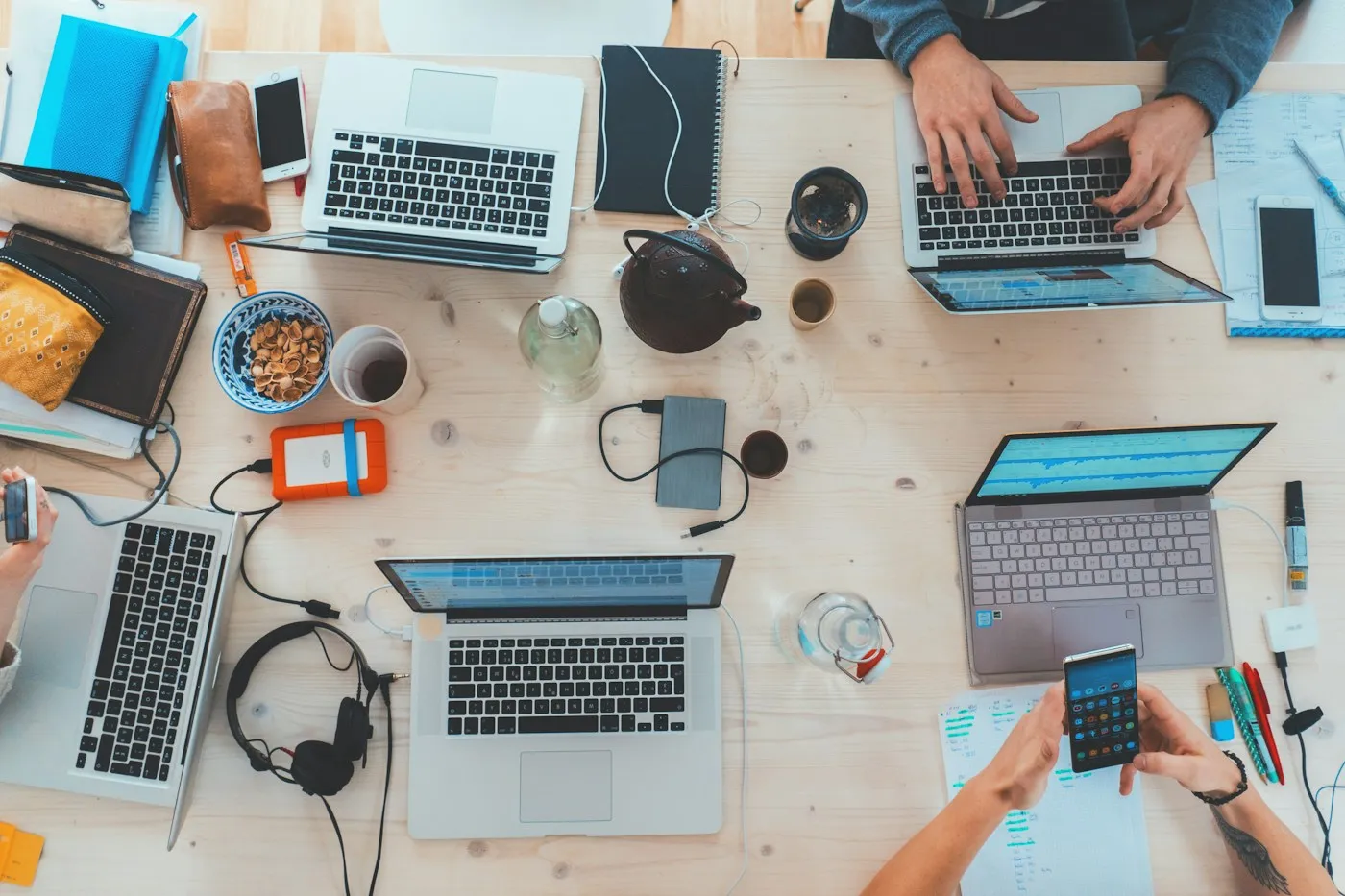 Work spread across laptops, notebooks, and phones on a shared table